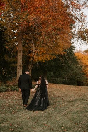 Two figures in dark formal wear walk together on a hill during peak fall foliage season.