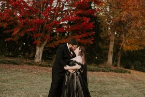 A romantic autumn photoshoot featuring a couple in black formal wear surrounded by red maple trees.