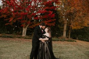 A couple shares a tender moment during their fall photoshoot with red and orange trees in the background.