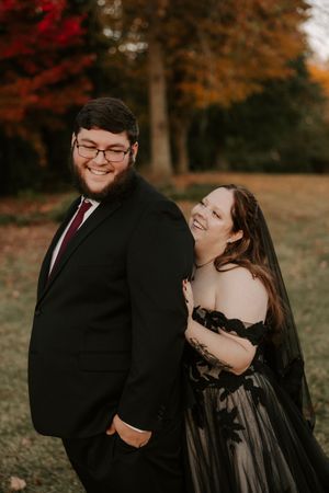 A romantic autumn photoshoot with a couple in black formal wear laughing together.