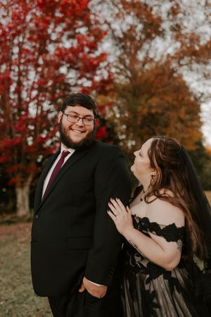 A couple shares laughter during their fall photoshoot with vibrant red maple trees in the background.