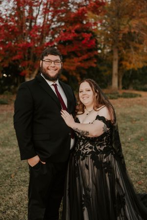 A couple poses together in formal wear during their fall outdoor photoshoot with red maple trees.