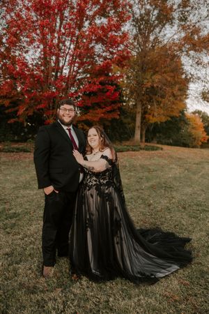 A couple in formal attire poses romantically against vibrant autumn foliage during a fall photo session.