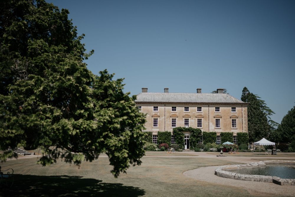 Elegant Georgian country house wedding venue surrounded by mature trees under a clear blue summer sky.