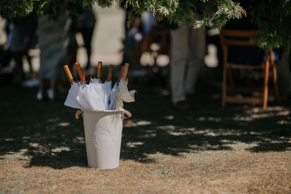 White bucket with umbrellas and hand fans for wedding guests at an outdoor summer ceremony.