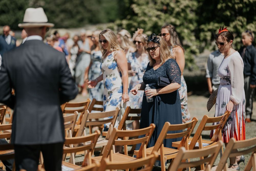 Wedding guests finding their seats at an elegant outdoor ceremony with wooden chairs.