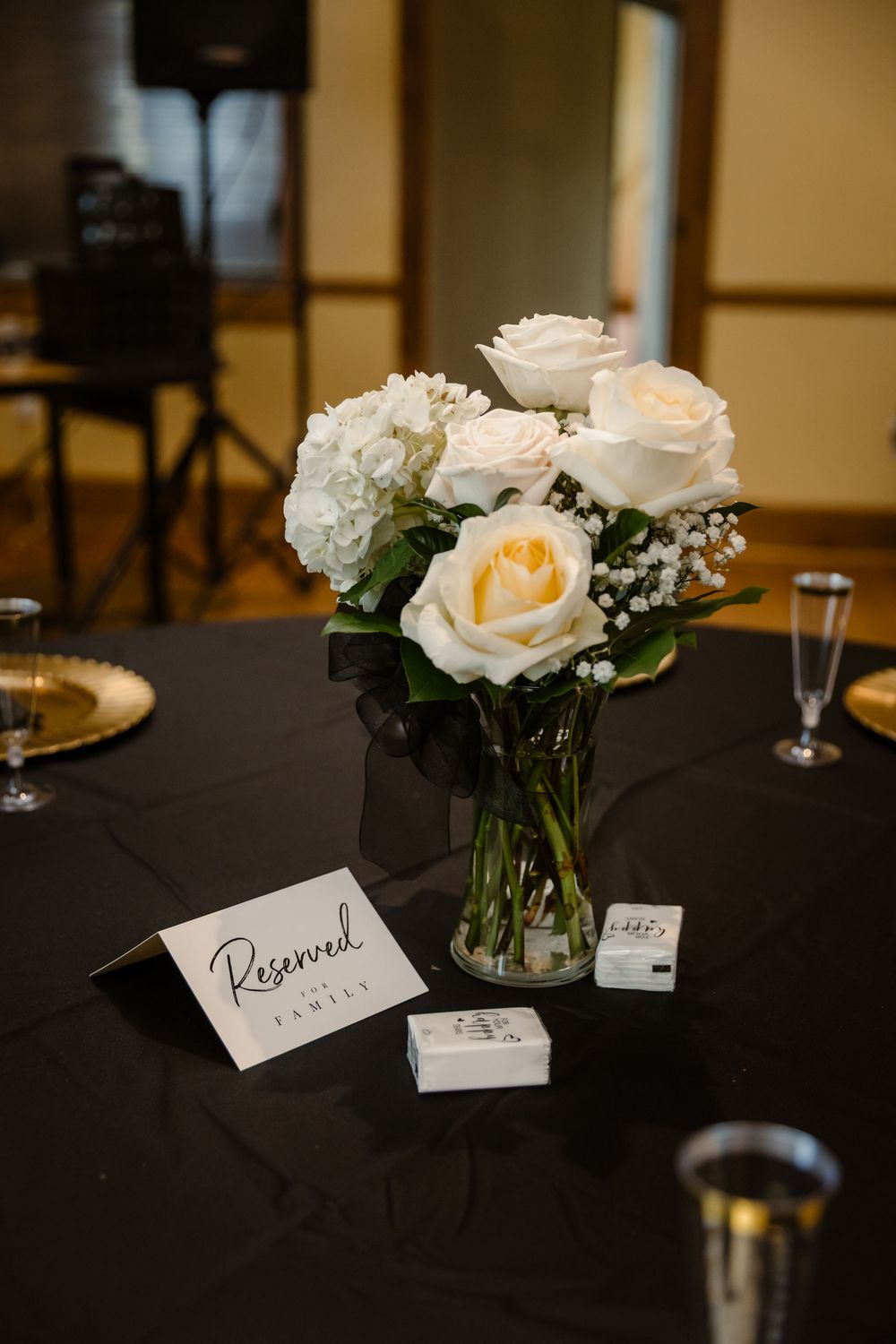 White roses and floral centerpieces with reserved table cards on black tablecloths at an elegant event setting.
