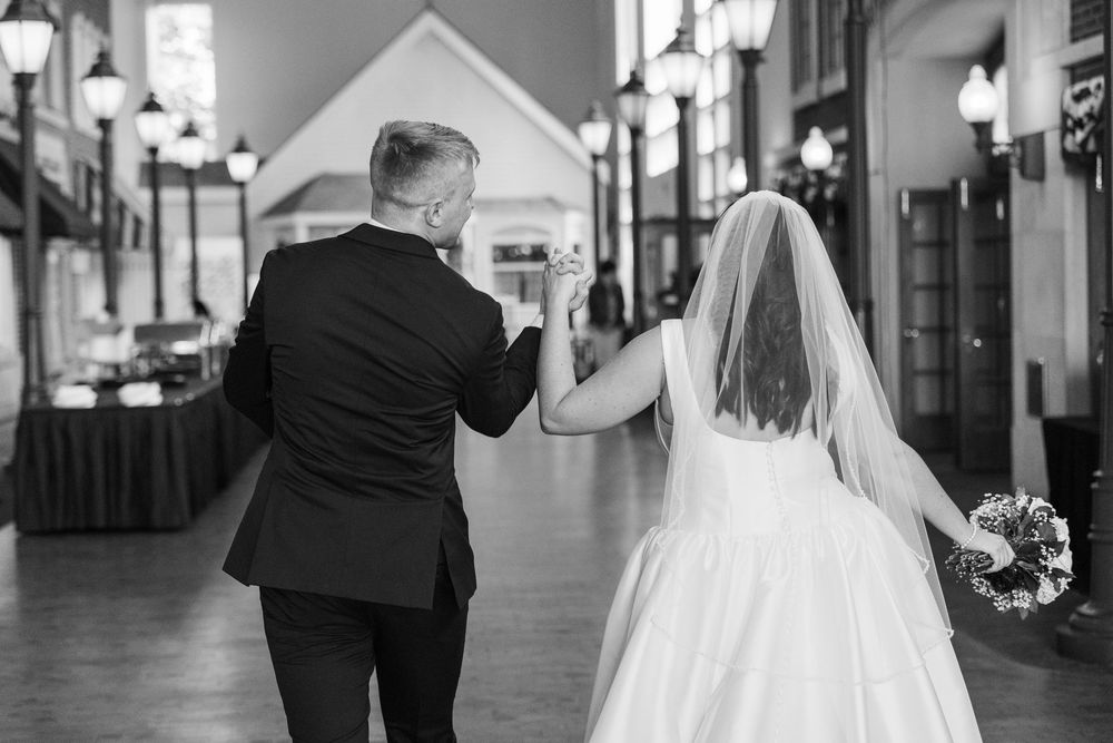 A black and white wedding photo shows a couple walking down a street lined with lanterns and storefronts.