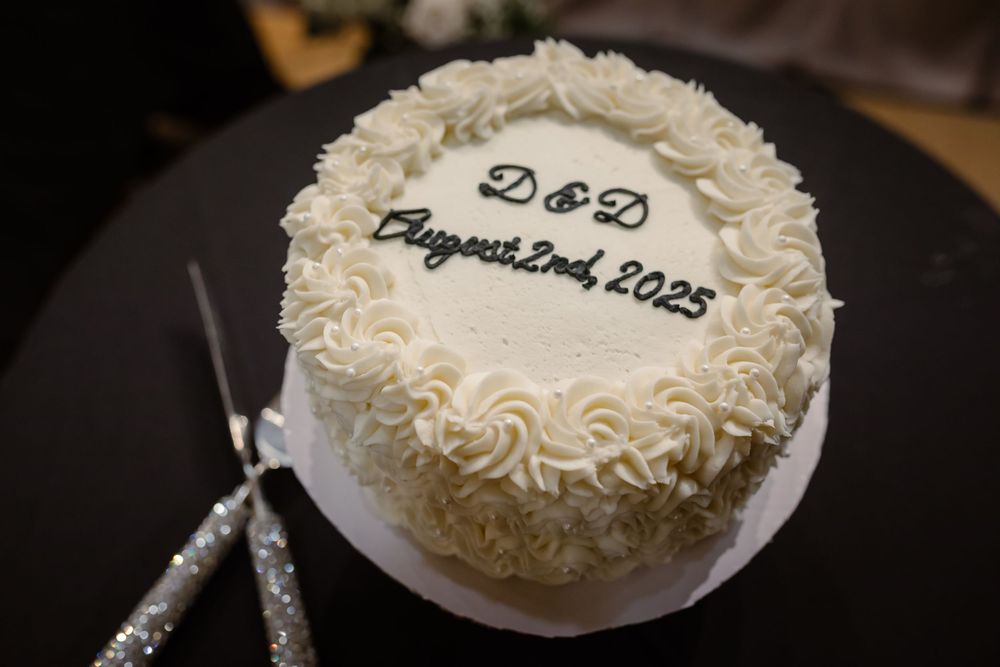 White frosted wedding cake with delicate piped rosettes and swirls displayed at a reception venue.