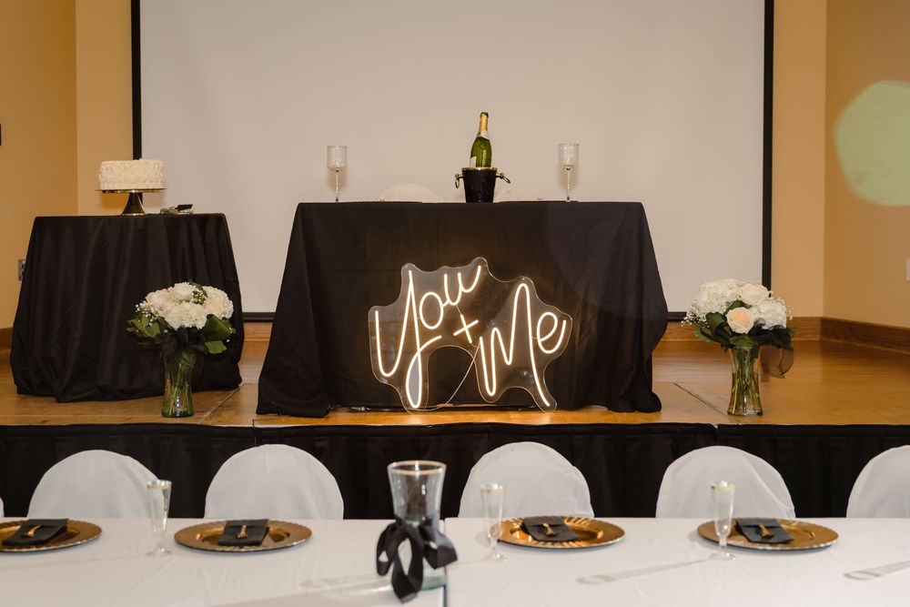 Wedding reception head table with illuminated Love sign, champagne bottle, white flowers and place settings.