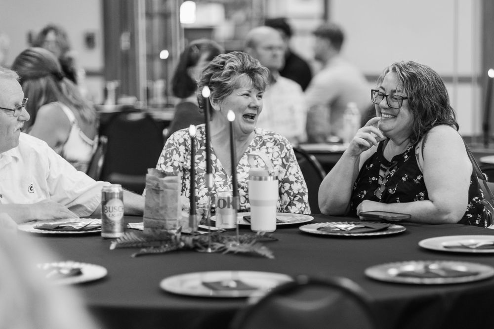 Black and white photo showing people seated at tables in what appears to be a dining hall or cafeteria setting.