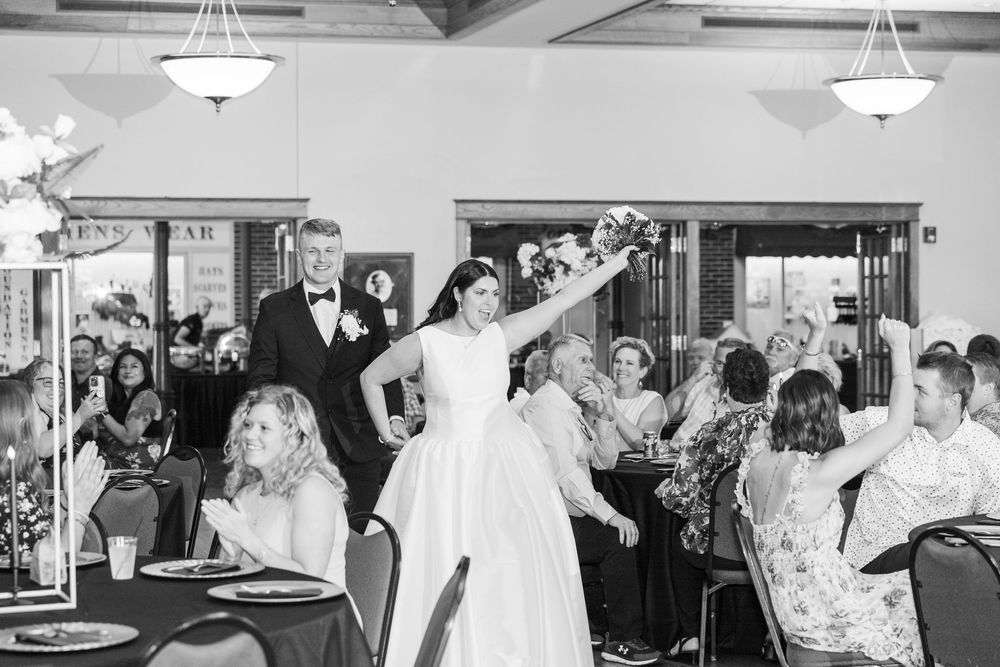 A group of wedding guests dancing and celebrating on a dance floor at an indoor reception venue.