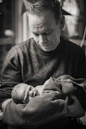 Förlossningsfotografering vid hemfödsel i Stockholm. Pappan håller det nyfödda barnet och ser på det med kärlek.