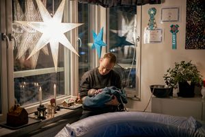 Förlossningsfotografering vid hemfödsel i Stockholm. Pappan håller det nyfödda barnet och ser på det med kärlek. Adventsstjärna i fönstret.