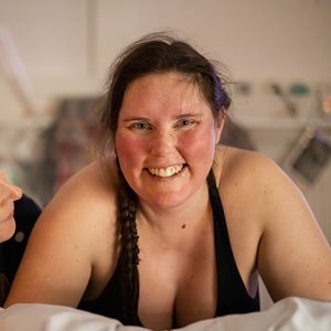 Förlossningsfotografering Södertälje BB. Glad, rosig kvinna ser in i kameran i en värkpaus