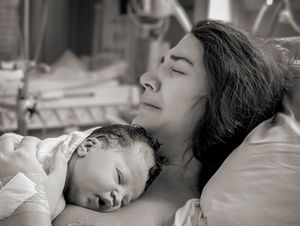 Förlossningsfotografering på Karolinska Solna. Nybliven mamma gråter av lycka medan hon ligger med sin bebis på bröstet