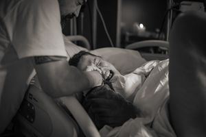 Förlossningsfotografering på St Görans sjukhus förlossning. Kvinna tar i och man ser smärtan i hennes ansikte under värken.