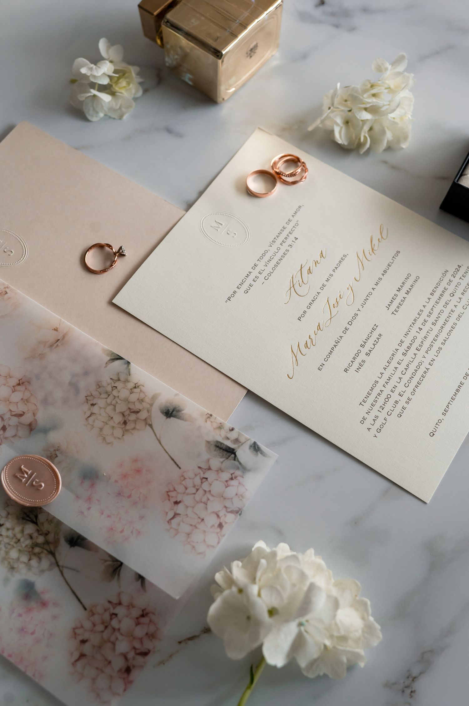 Wedding invitations with rose gold details and white flowers on marble surface.