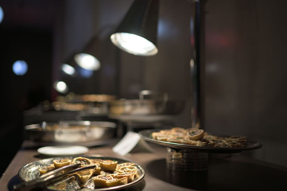 Illuminated restaurant table with plates of food under warm lamp lighting in dark ambient setting.