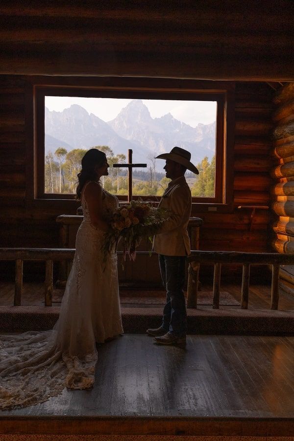 Silhouettes dance in a rustic log cabin with large windows framing a mountain landscape.