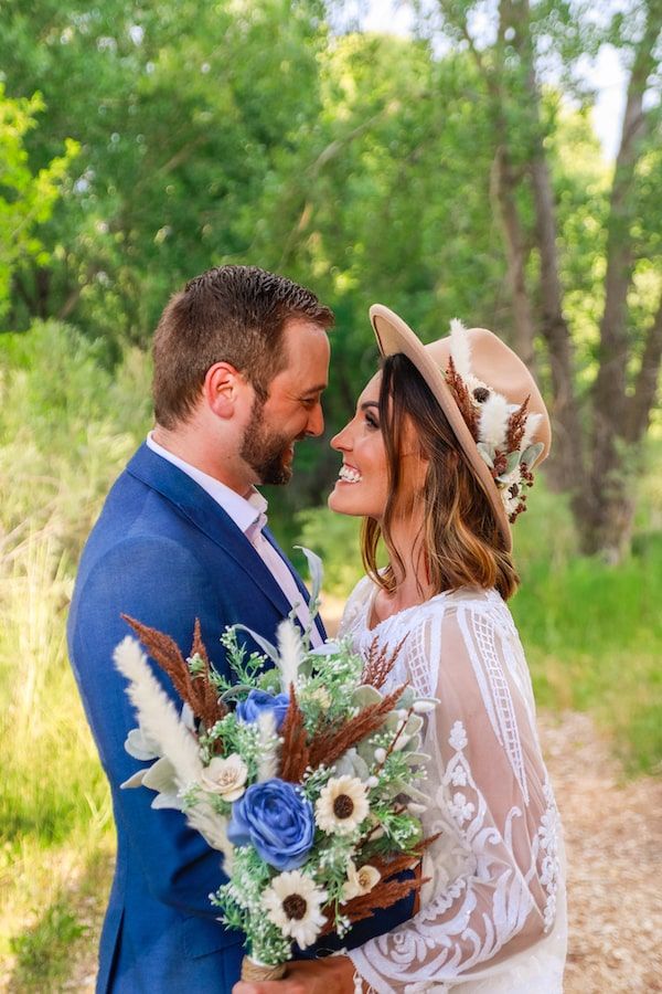 Romantic outdoor wedding photos showing couple embracing in a sunlit wooded area with blue and white floral bouquet.