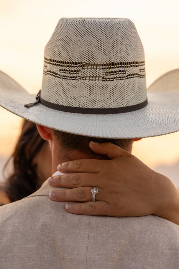 A close-up view of a white straw hat and an engagement ring during a sunset photoshoot.