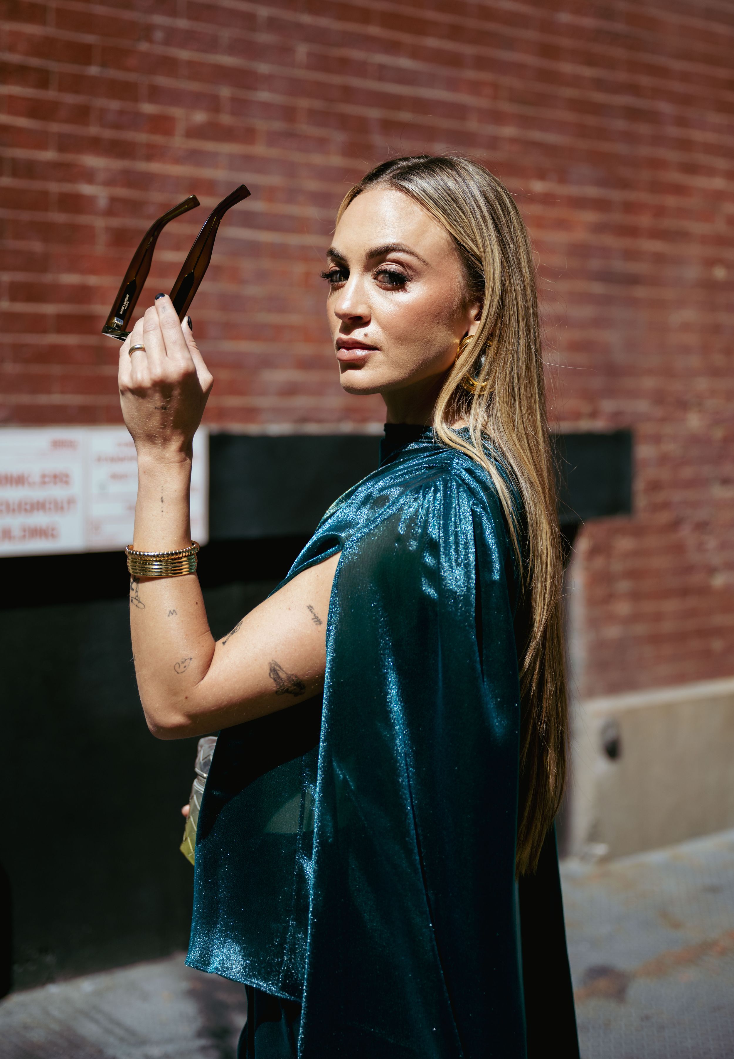 A sequence of fashion portraits showing a person in a metallic blue top against a brick wall background.