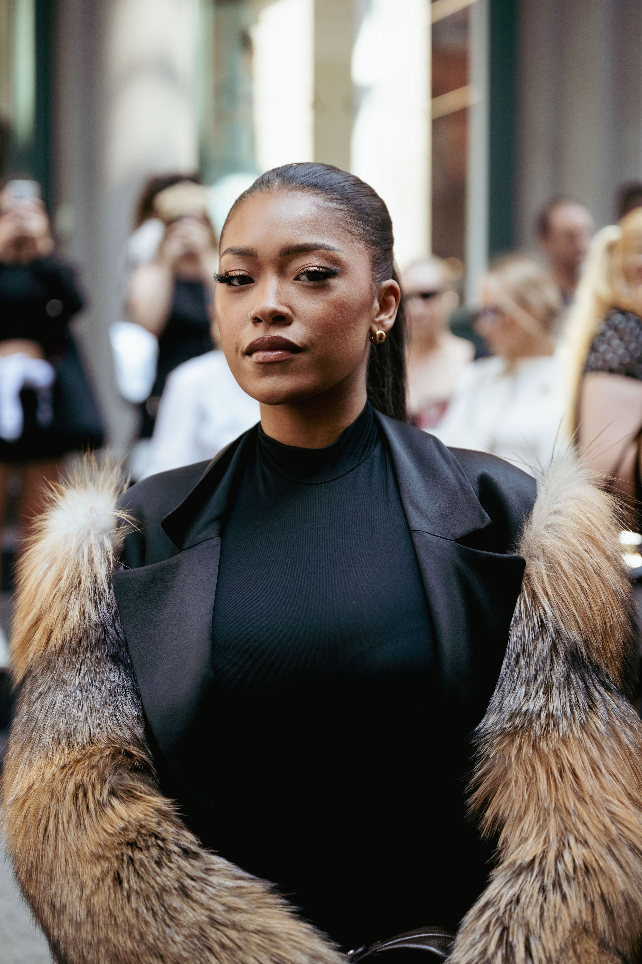 A fashion portrait featuring a black turtleneck and brown fur-trimmed coat in an urban setting.