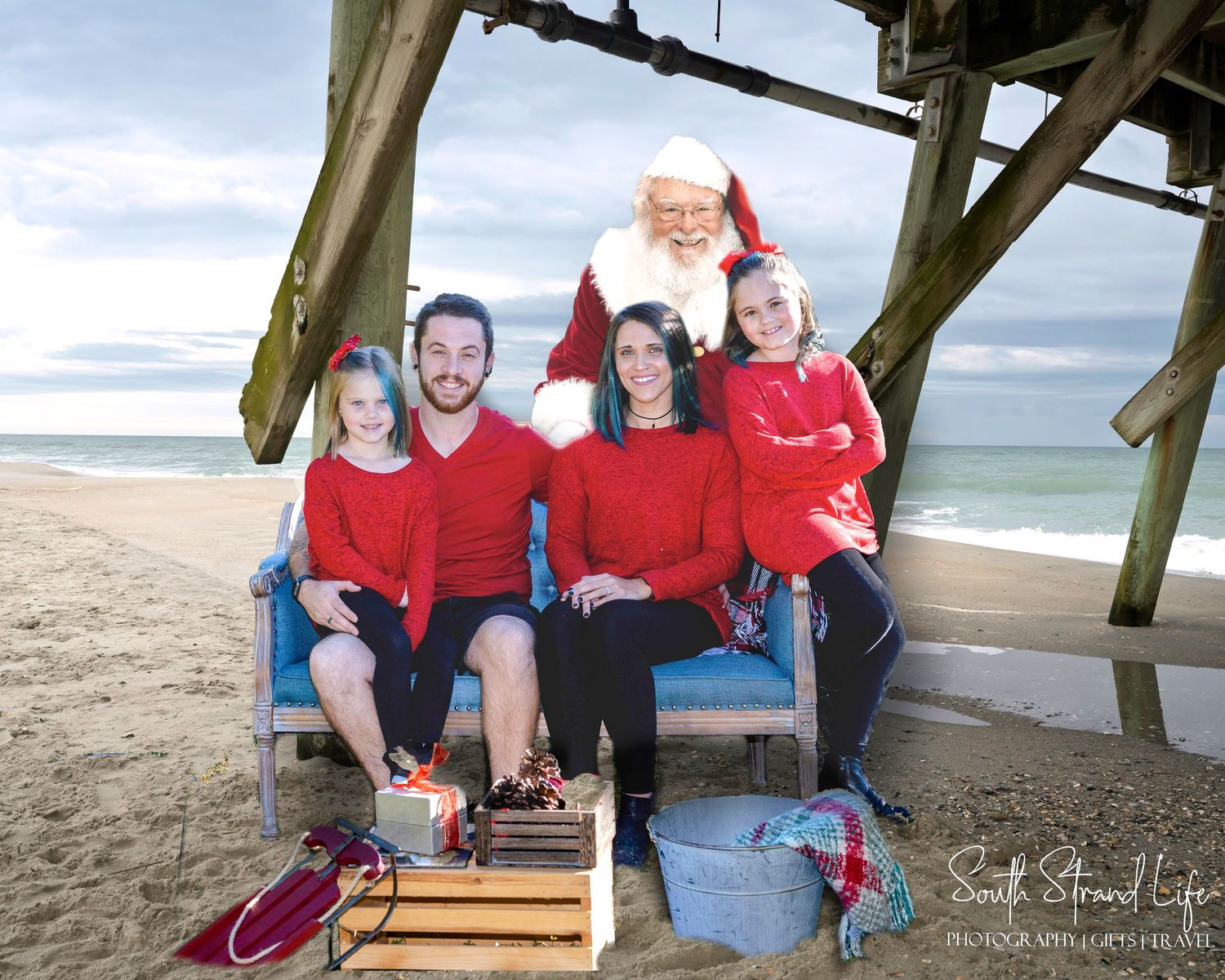 A group wearing red shirts poses together on a wooden pier at the beach during a family photo session.