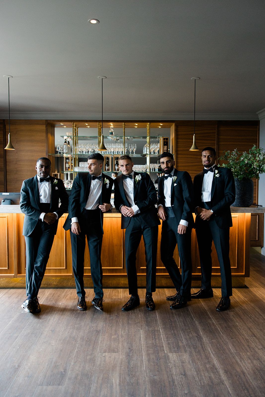 People in formal attire dancing joyfully on a wooden deck with glass walls and nature views in the background.