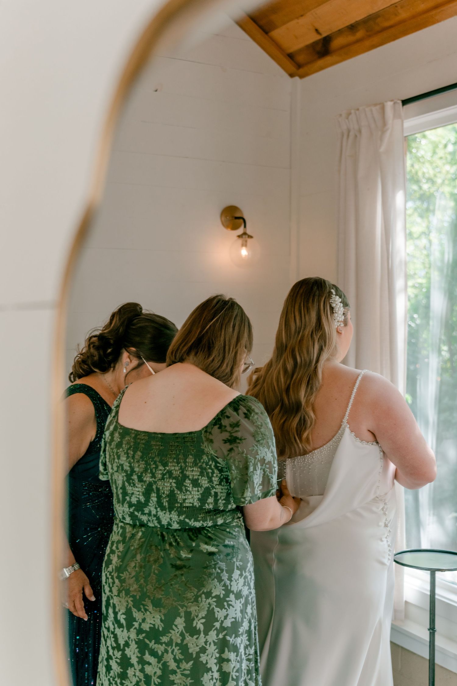 A bride in a white dress poses near a window with natural light streaming in, creating a soft, romantic atmosphere.