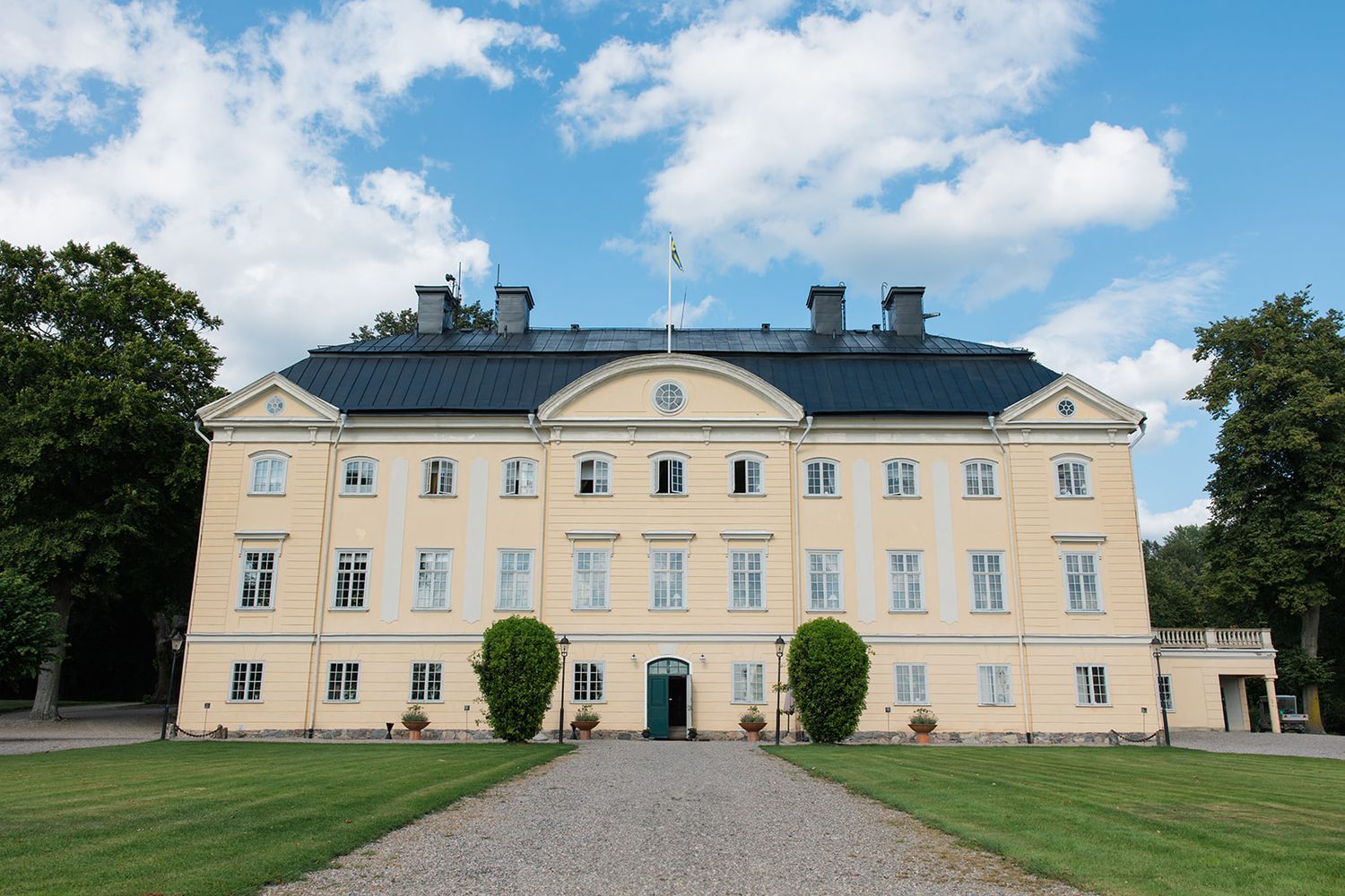 Aerial view of a grand white manor house with symmetrical gardens, side buildings and tree-lined grounds in Estonia.
