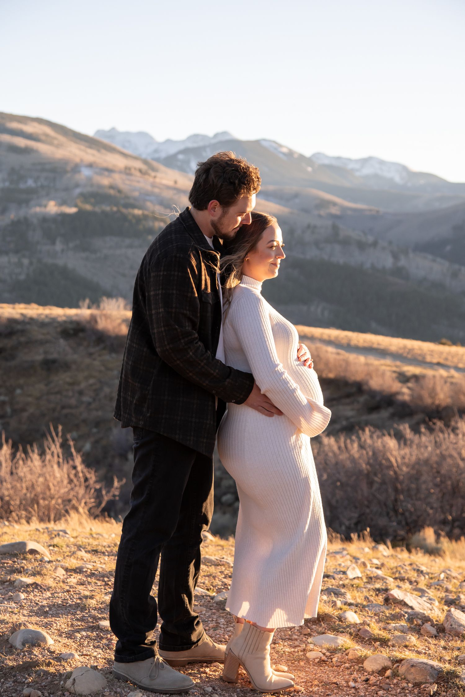 A fashionable couple shares a tender moment on a mountainside during sunset for a maternity photo session in Vail Colorado