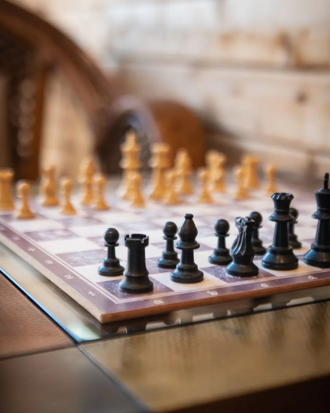 A chessboard set up for play, lit by warm natural light in a cosy indoor space.