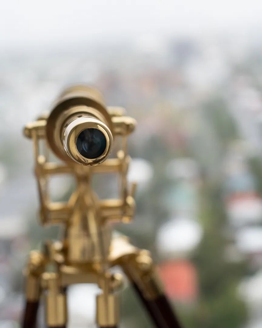 Brass telescope pointing toward a blurred cityscape in soft daylight.