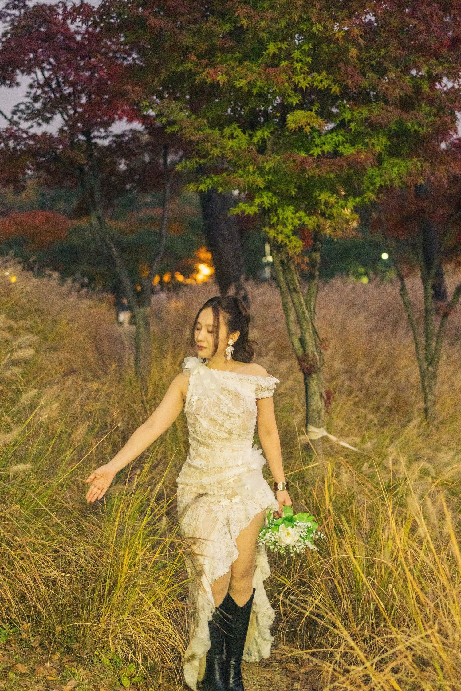 A person in a cream-colored dress walks through tall golden grass with autumn trees in the background.