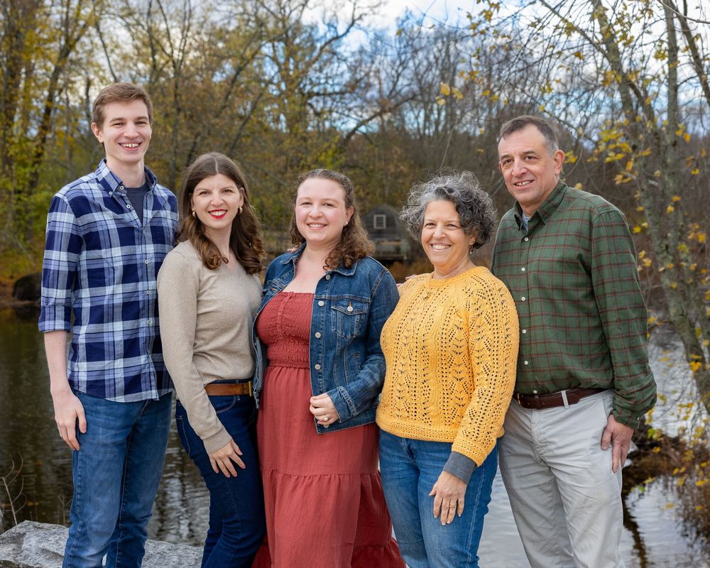 Parents and adult children wearing casual fall attire pose together outdoors with autumn trees in the background in Concord, MA.
