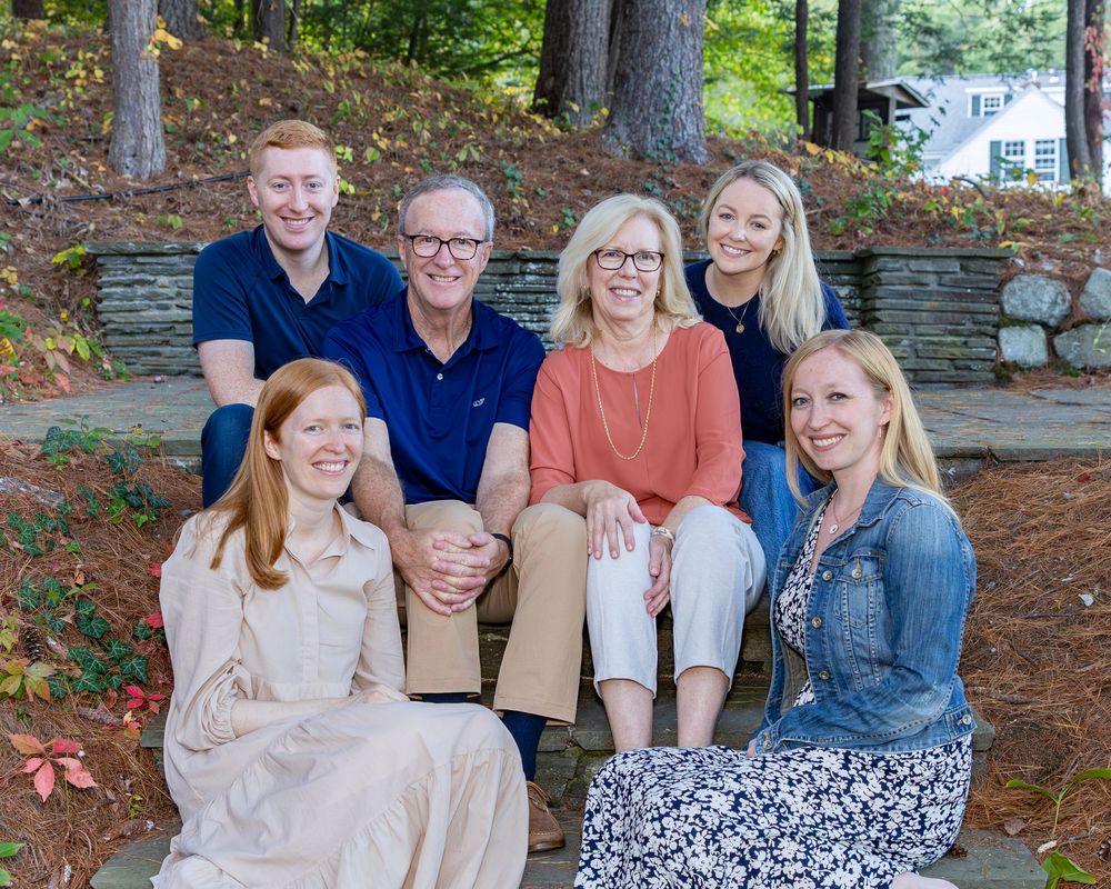 Parents with their adult children pose on steps during an extended family photo shoot with a stone wall behind them.