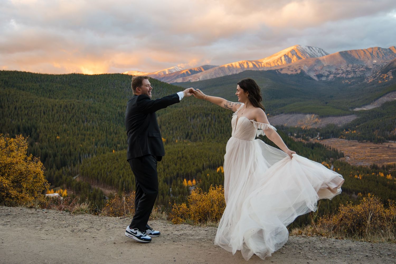 A couple dances together against a scenic mountain backdrop at sunset during their wedding celebration.