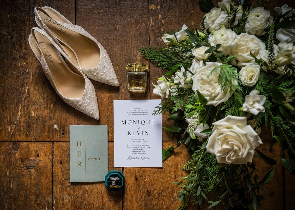 Wedding details including white roses, invitation cards, and bridal accessories on wooden surface.