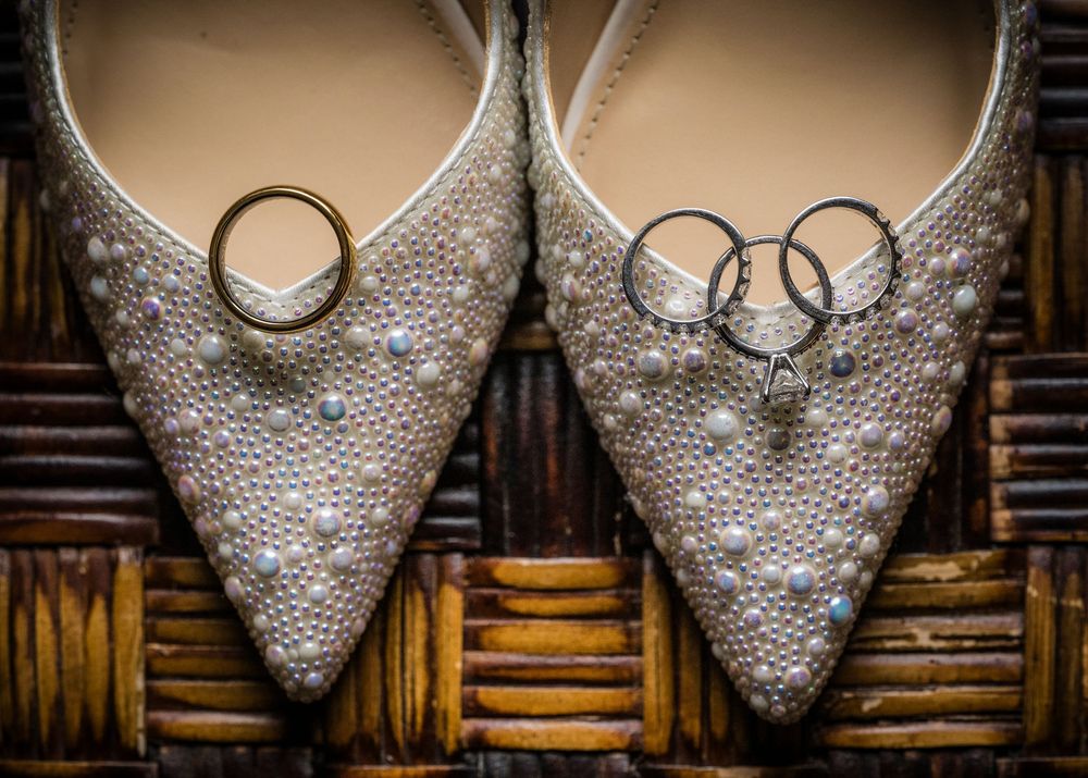 Sparkly bridal shoes with wedding rings arranged for detail photo on wooden background.