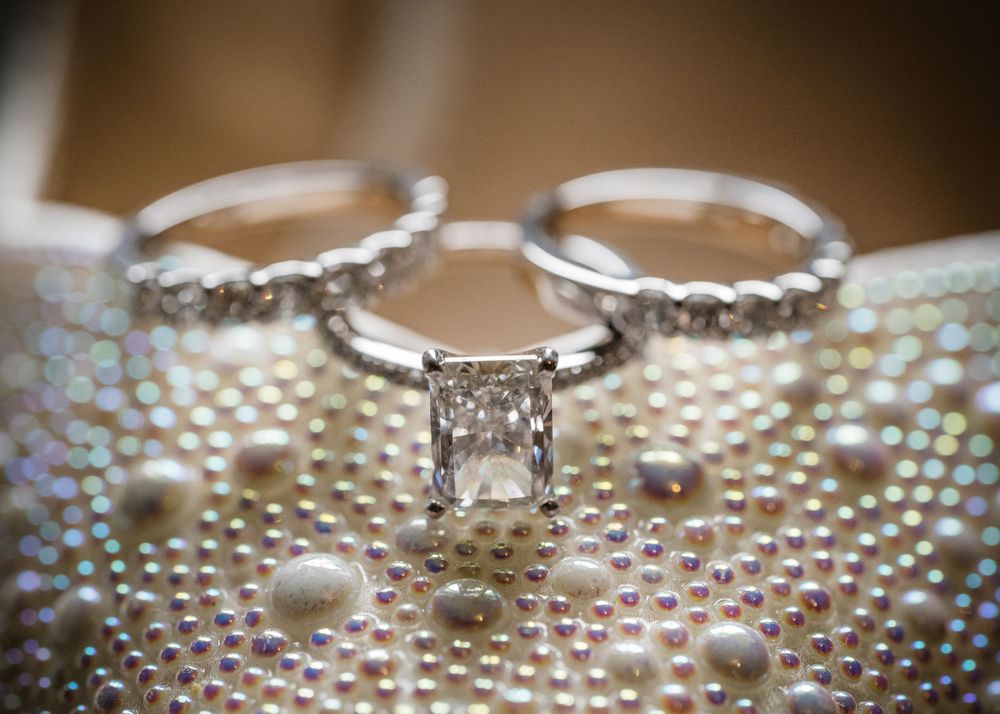 Diamond engagement ring and wedding bands photographed on iridescent beaded surface.