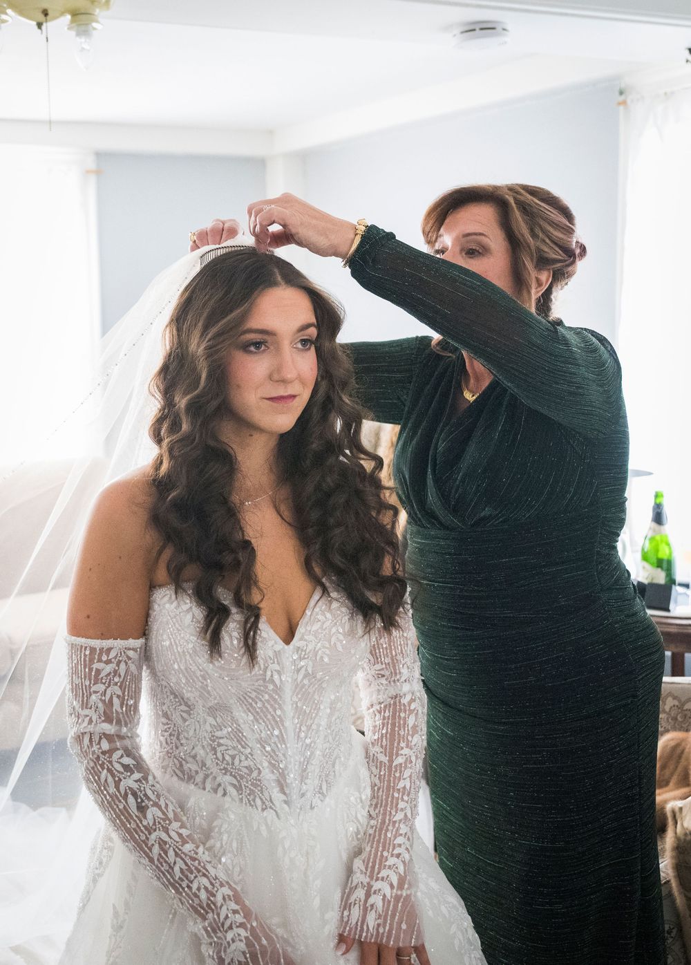 A bride in a lace wedding dress getting her hair styled in soft waves on her wedding day.