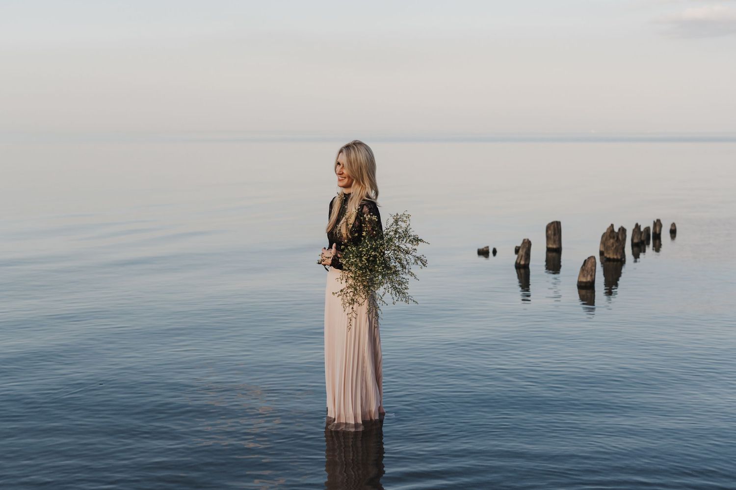 Michelle Hugill standing in calm lake water, holding a bouquet of wildflowers