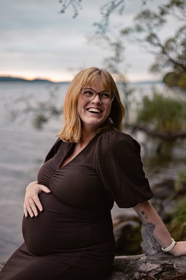 Gravidfotografering utomhus med en glad, gravid kvinna som tittar över axeln och skrattar