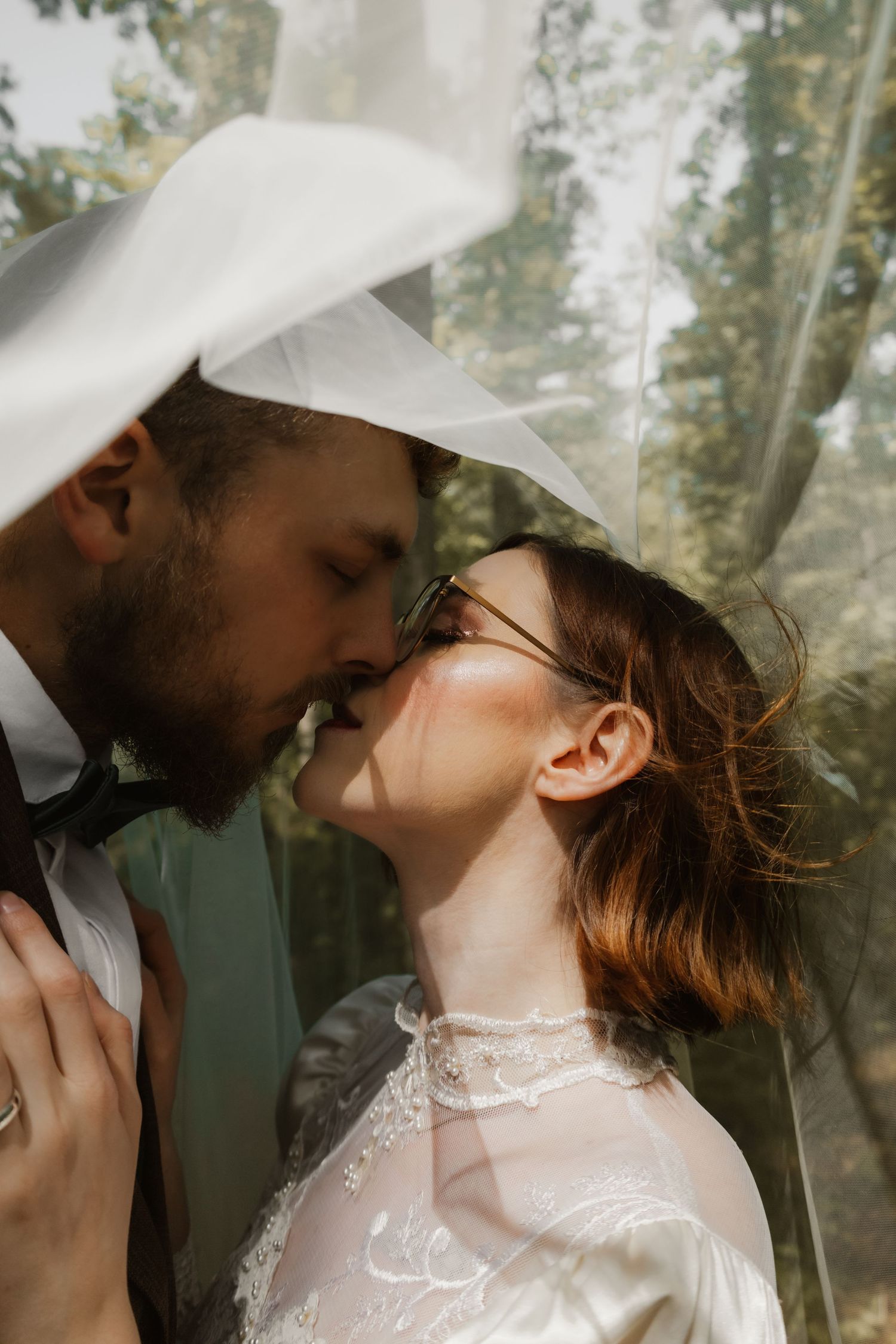 A romantic wedding couple shares intimate kisses in a dreamy forest setting with soft natural light.