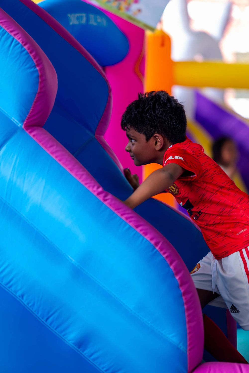 Young child climbing on a bright blue and pink inflatable bounce house obstacle course.