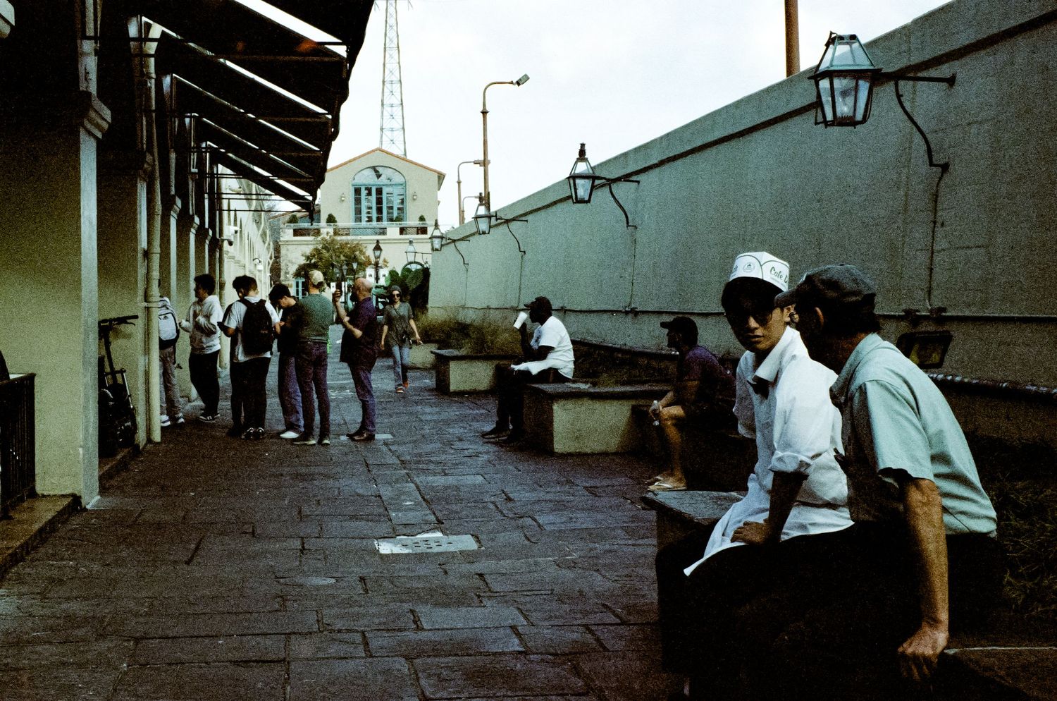 People relaxing along a covered walkway with white walls and lanterns.