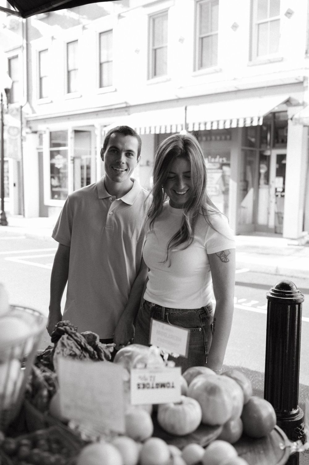 Casual couple shopping at an outdoor produce stand on a sunny urban street.