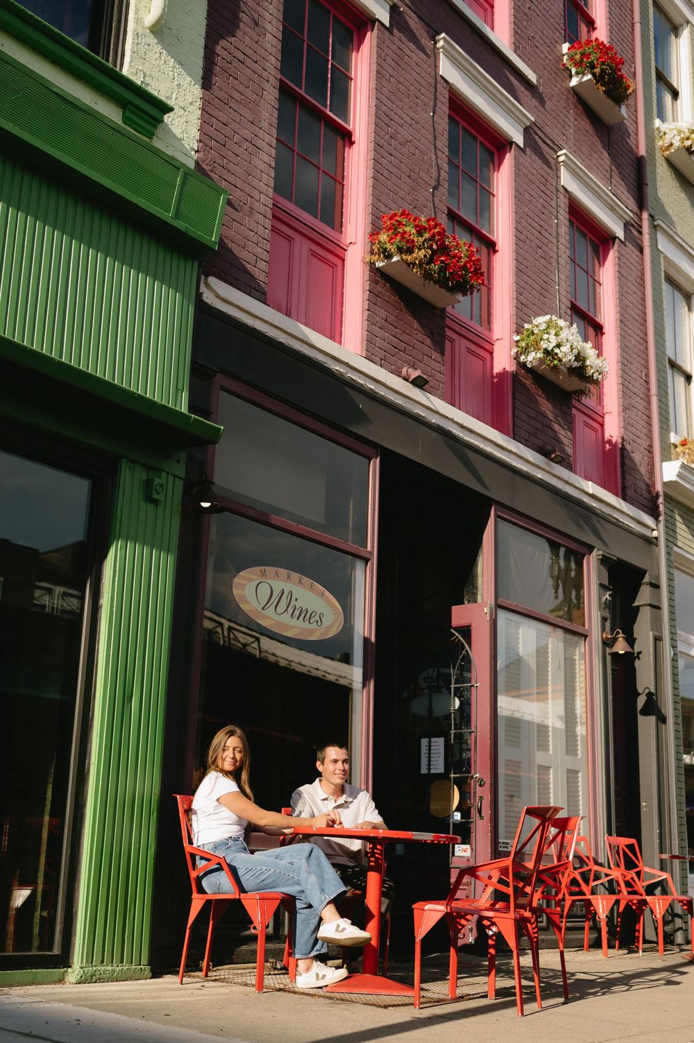Couple enjoying outdoor seating at a cafe with colorful brick buildings and red chairs.